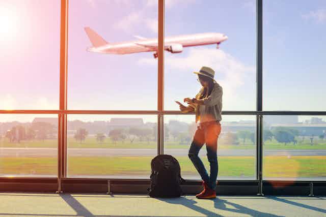 Young woman with backpack in airport departure lounge with plane taking off in background