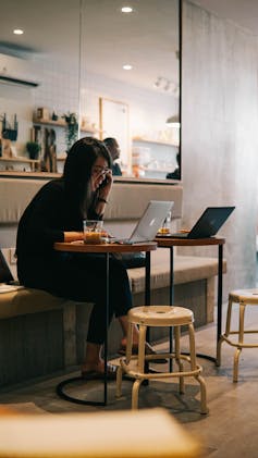 Busy woman sits at a cafe on her computer, talking on the phone.