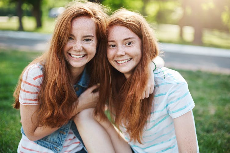 Twin women hug outside in the sunshine.