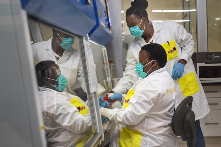 Duas pessoas em jalecos, luvas e máscaras em um laboratório