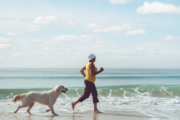Woman jogs along the beach with her dog.