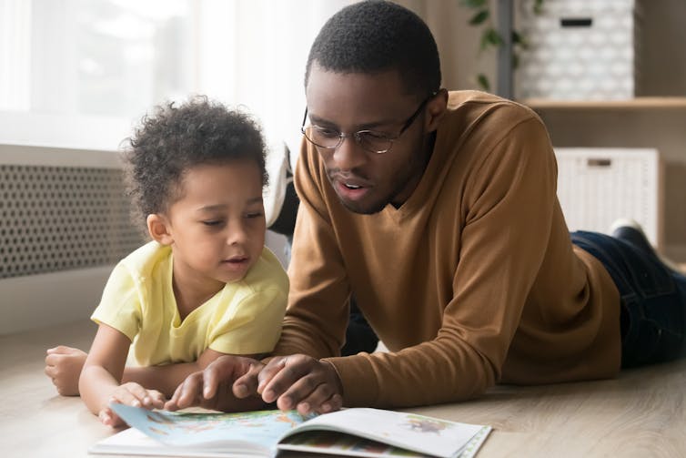 Father and son lying on floor looking at book