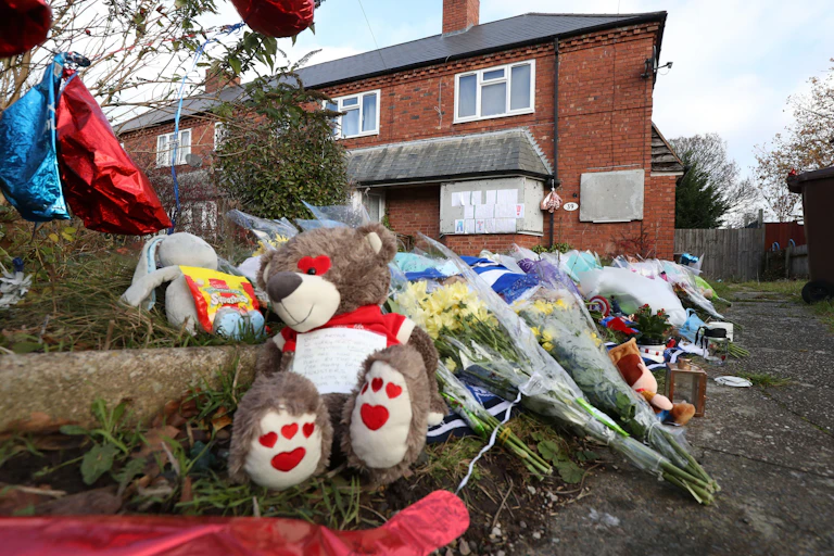 Close-up photo of teddy bears and flowers on the ground in front of a house