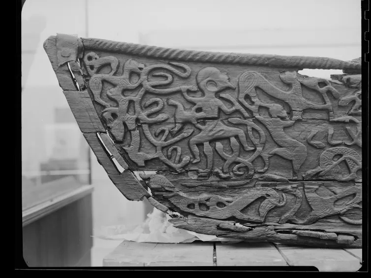 A wooden carving depicting a body in a snake pit.