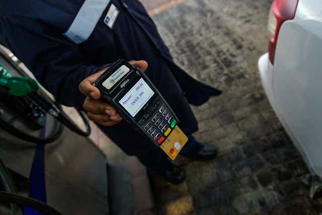 A petrol attendant holding a card machine while processing a bank card payment at a petrol station.