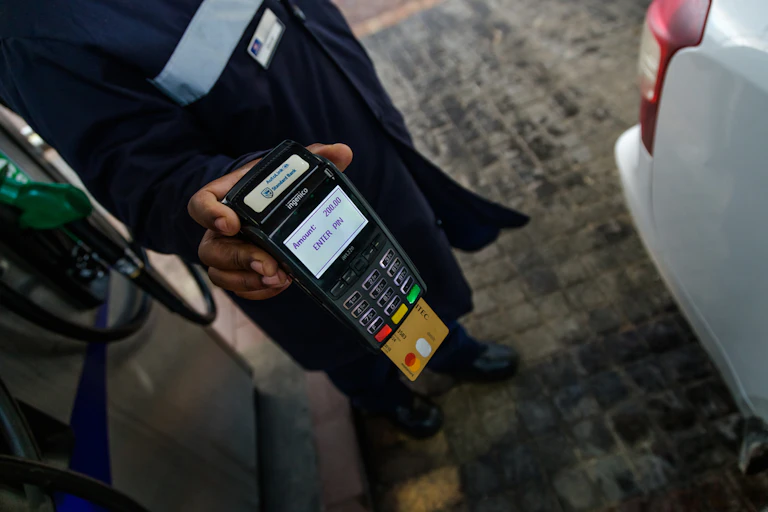 A petrol attendant holding a card machine while processing a bank card payment at a petrol station.