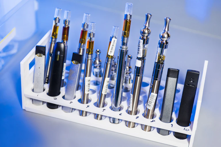 Une sélection de vapoteuses sont disposées sur un portant de tubes à essais.