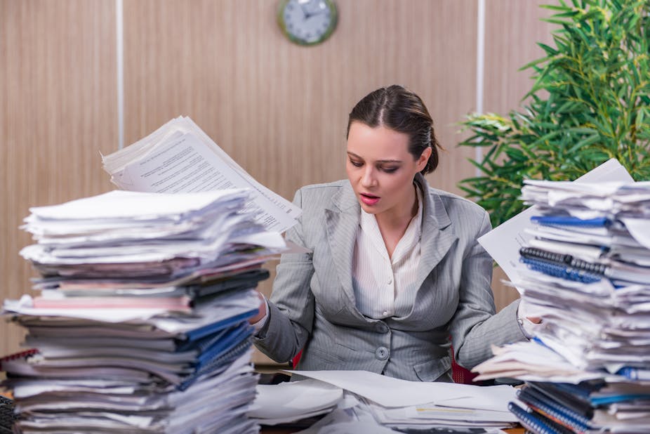 A woman surrounded by stacks of paper.