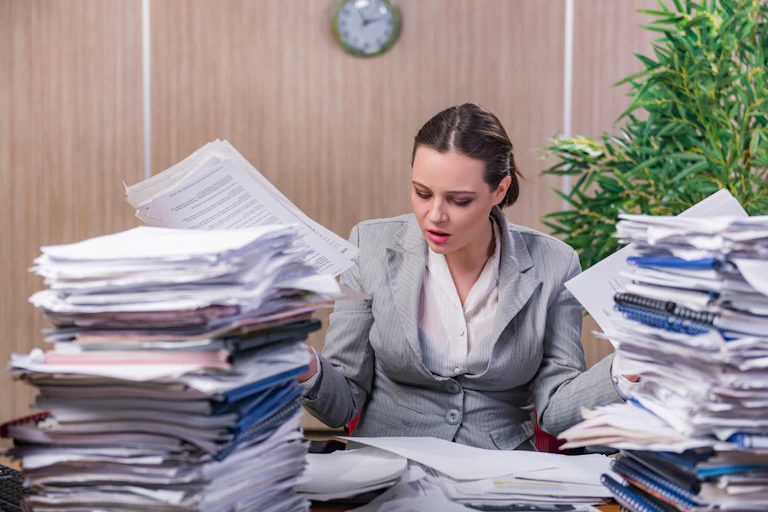 A woman surrounded by stacks of paper.
