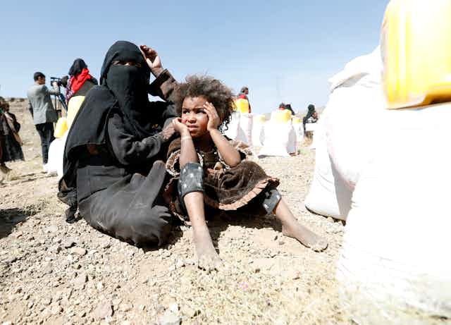 A woman in a burqa holds a young boy with aid workers in the background.