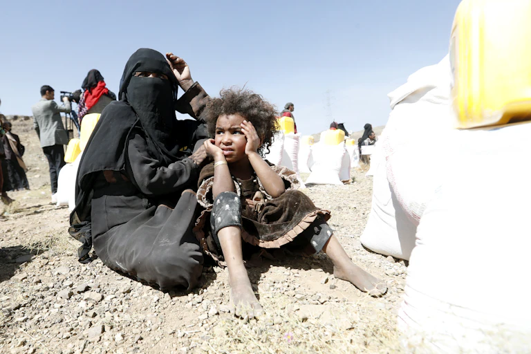 A woman in a burqa holds a young boy with aid workers in the background.