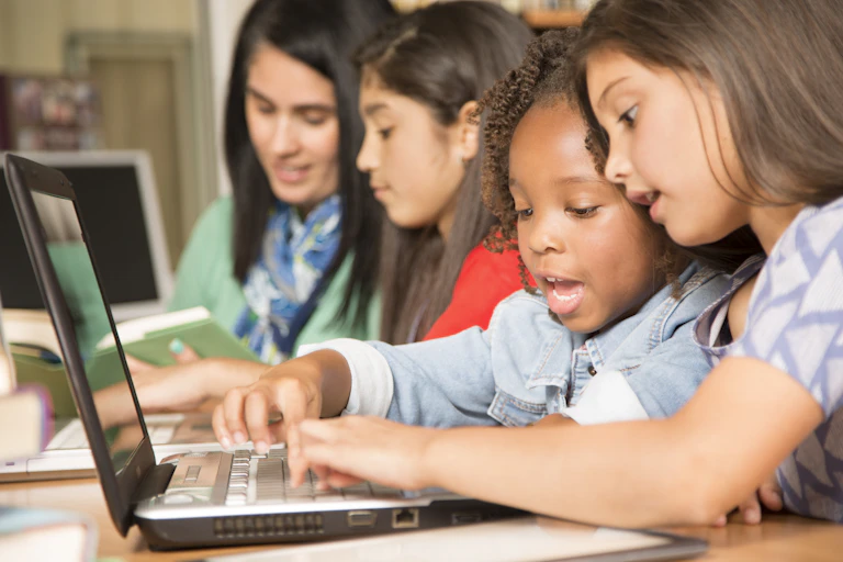 Two girls use a laptop together.