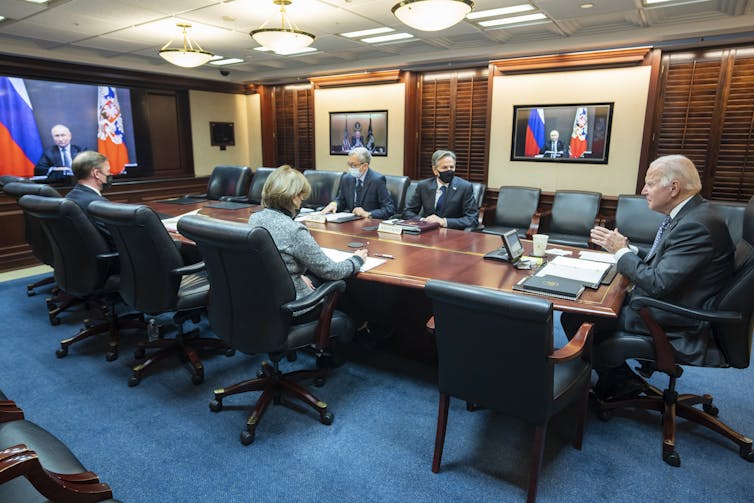 US President Joe Biden sits at a large conference table, surrounded by four officials, including US Secretary of State Tony Blinken, as he speaks with Russian president Vladimir Putin on video call.