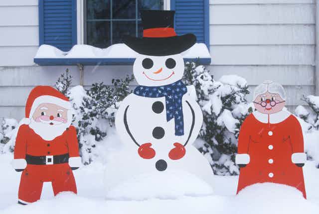 Cutouts of Santa Claus, a snowman and Mrs. Claus on a snow-covered lawn.