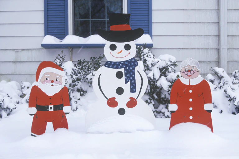 Cutouts of Santa Claus, a snowman and Mrs. Claus on a snow-covered lawn.