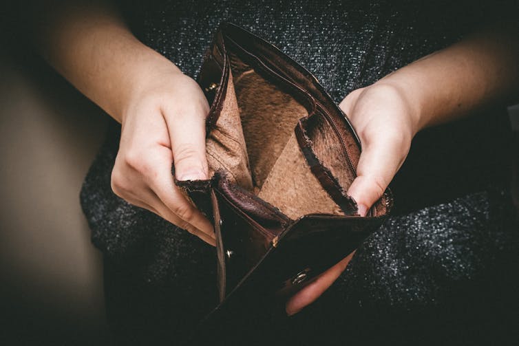 A person holds an empty wallet open, it is a close up of the hands and the wallet.