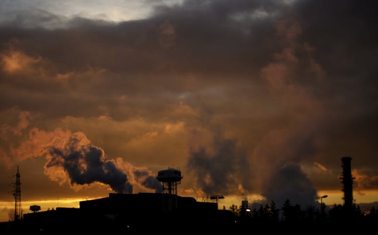 Silhouette of gases rising from an industrial complex with a golden sunset.