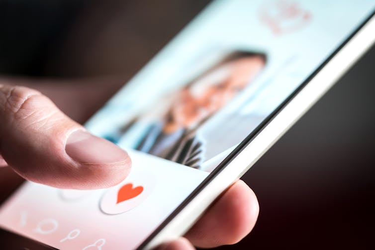 A hand is holding a phone, you can see them swiping left/right on a dating app