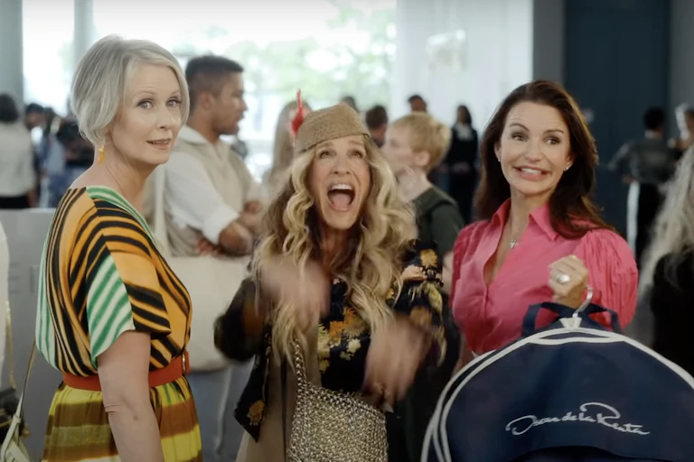 Three women dressed in designer clothes look at the camera excitedly