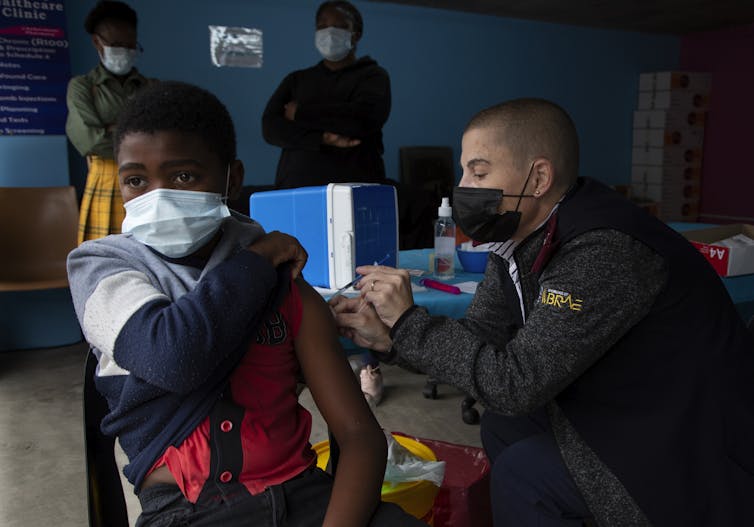 Un jeune garçon se fait vacciner par un homme portant un masque