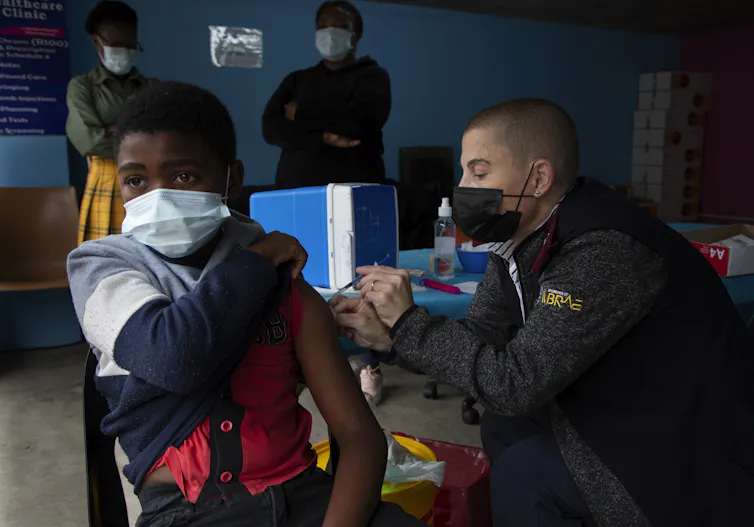 Un jeune garçon se fait vacciner par un homme portant un masque