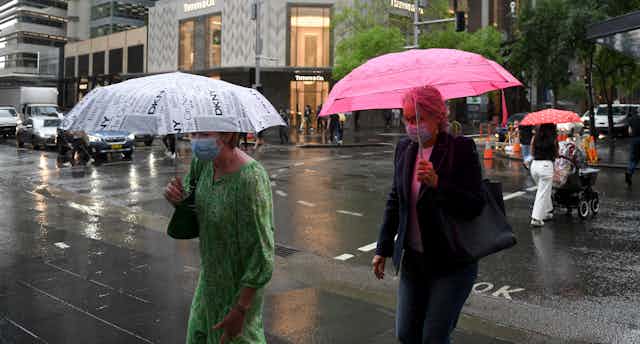 pedestrians with umbrellas cross wet street