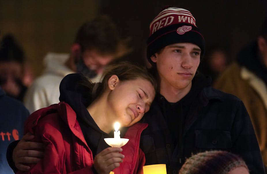 A young woman holding a candle cries as a young man puts his arm around her.