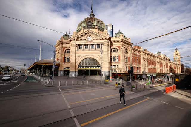 Masked person walking in front of quiet Flinders Street Station