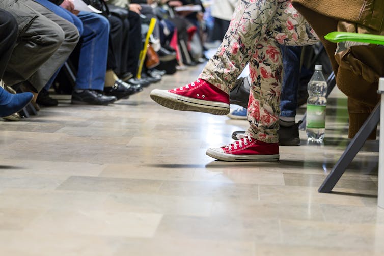 Young person in pink shoes sits in a waiting room.