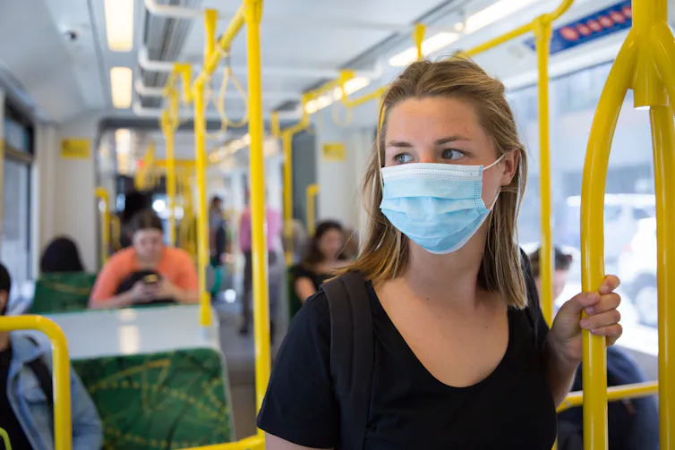 Young masked woman standing on a train