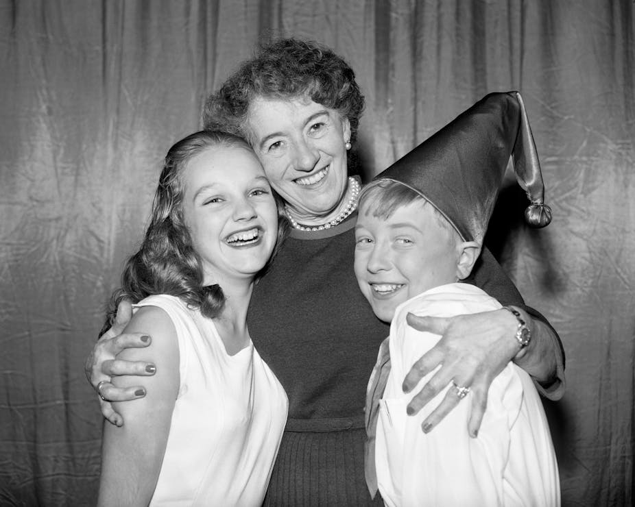 Woman poses with two children, one in a hat.
