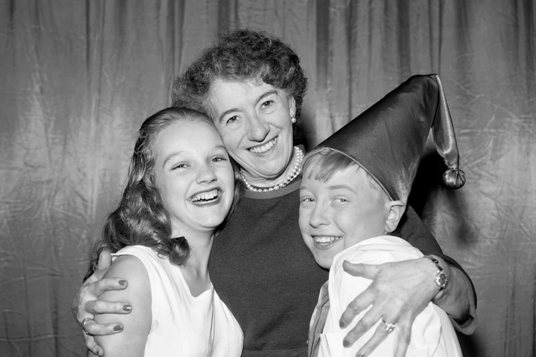 Woman poses with two children, one in a hat.