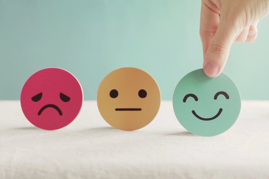 Three paper cutouts of a sad, neutral and happy face to illustrate mental health.