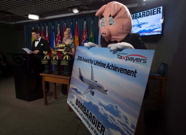 An awards ceremony, a pig holds a sign that reads 'canadian taxpayers federation 2016 lifetime achievement award'