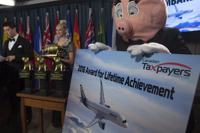 An awards ceremony, a pig holds a sign that reads 'canadian taxpayers federation 2016 lifetime achievement award'