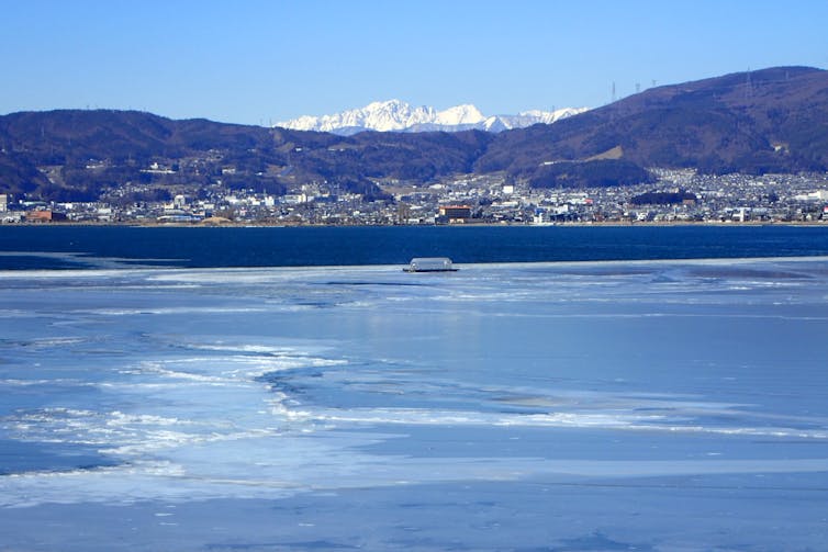 The view of the ice cover and ice ridges on Lake Suwa, Japan, with the mountains in the background.