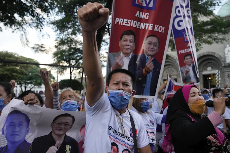 A man with a mask below his nose stands with his fist in the air, he us flanked but hundreds of other people