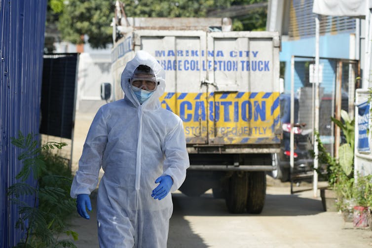 A worker wearing protective gear walks ahead of a truck that reads 'caution'