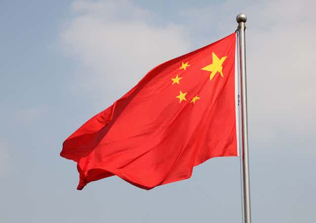 The Chinese flag flutters against a light blue sky.