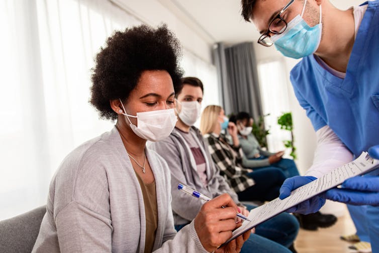 A doctor and a patient, wearing masks, filling out a vaccine consent form