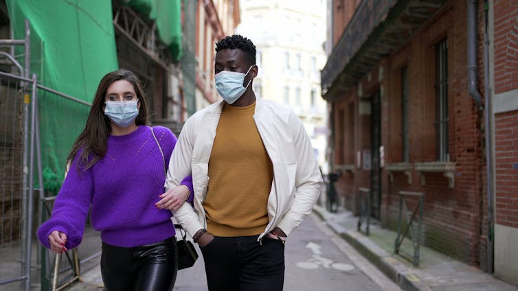 A Black man and a white woman walking down the street in masks