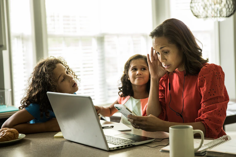 A woman trying to work on a computer at home while two kids bother her.