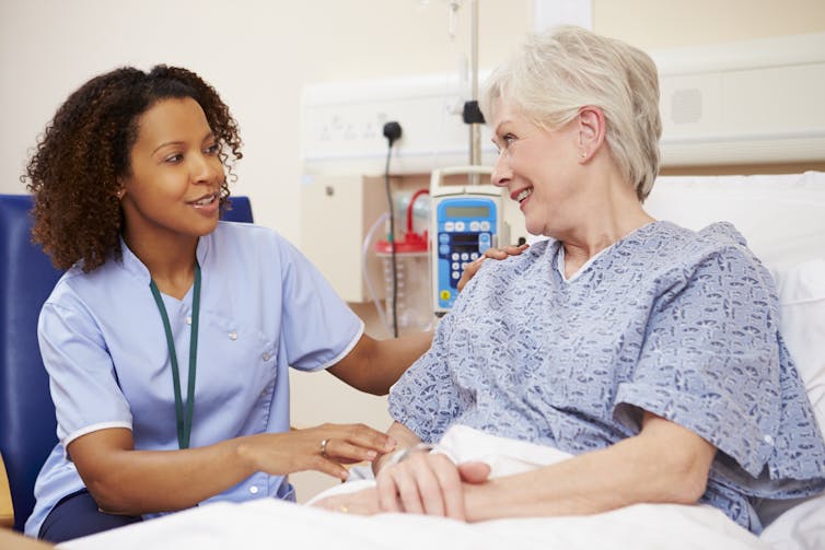 Nurse sitting by patient's bed in hospital