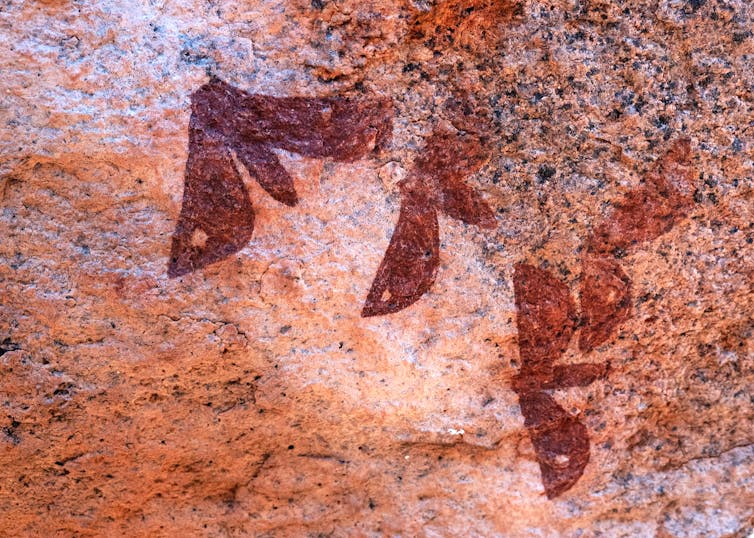 A rock drawing of four butterflies, in red, has spots on their extended wings.