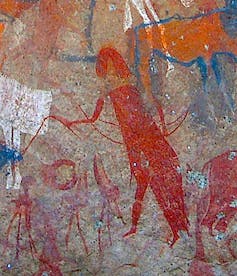 Drawing in red on a rock depicting a character in a cloak, moving forward, with an arm outstretched.  Around them are cattle and people.