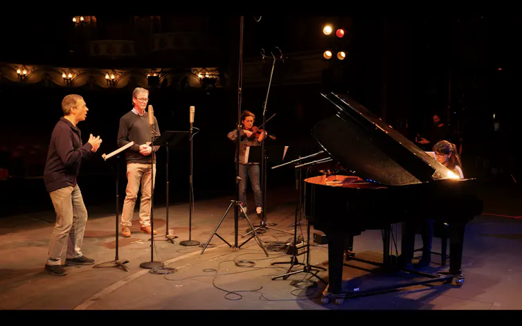 Four people on a stage playing musical instruments and singing.