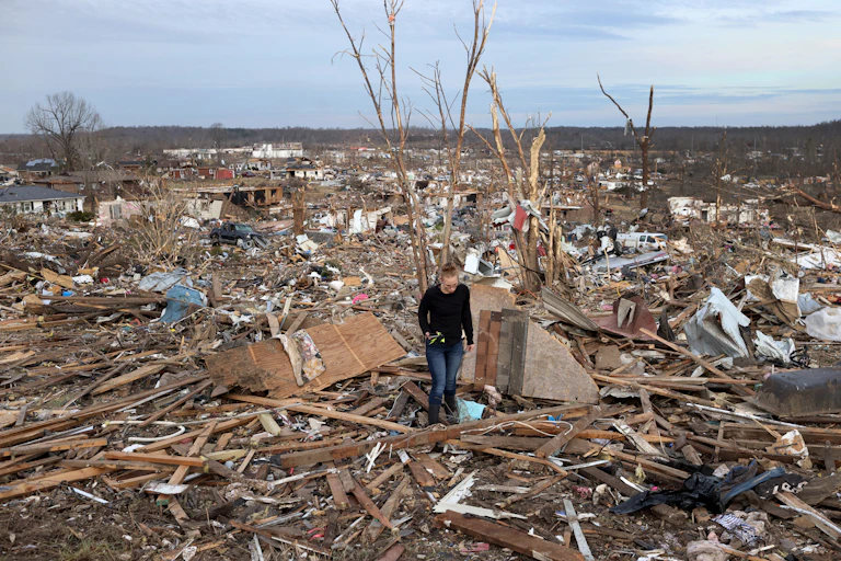 A woman rummages through wreckage.