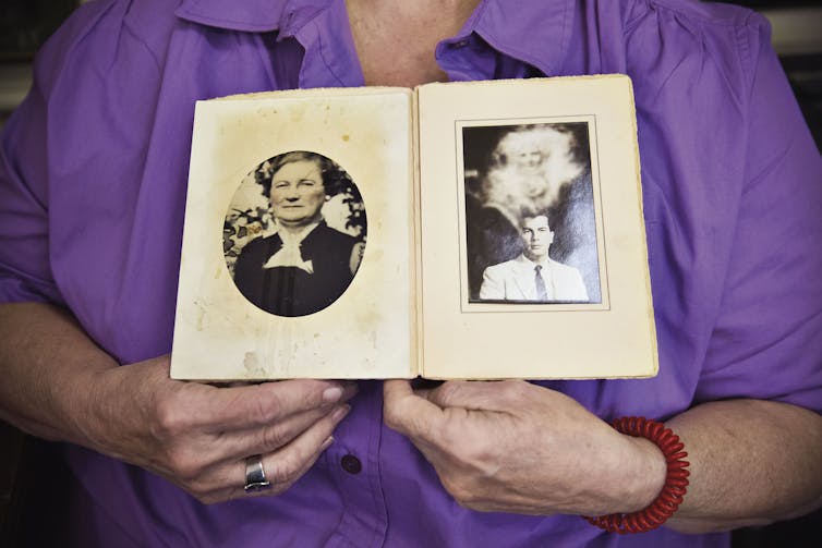 Woman holds photo album with two black and white portraits.
