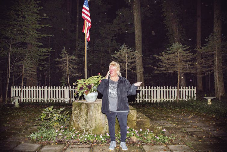 Woman stands before American flag with arms outstretched.