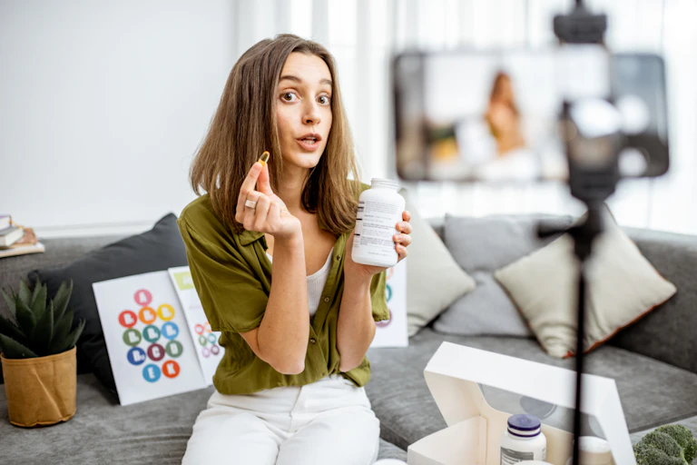 Young woman holding pill and pill container speaking to smartphone, spruiking vitamins
